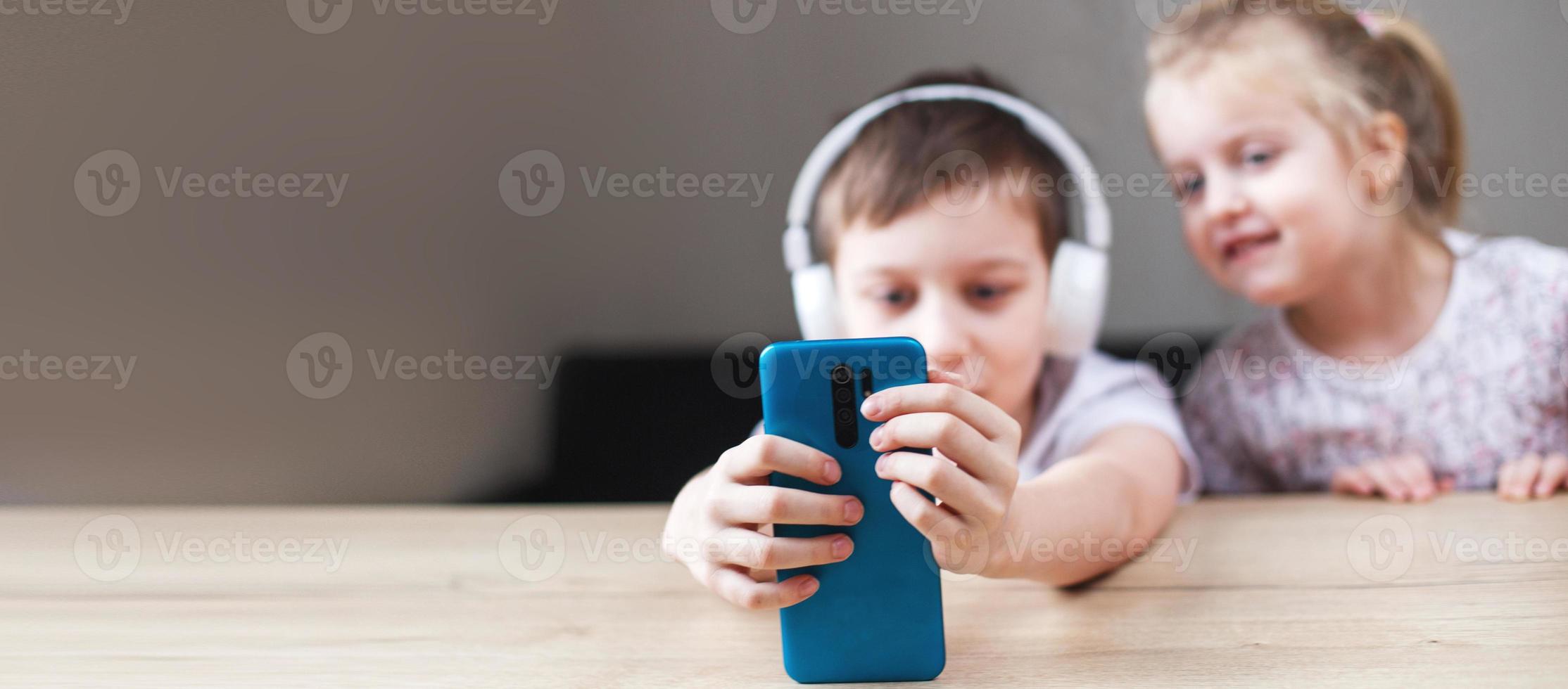 twee gelukkig kinderen spelen Aan de smartphone in koptelefoon. mensen, kinderen en technologie concept. banier foto