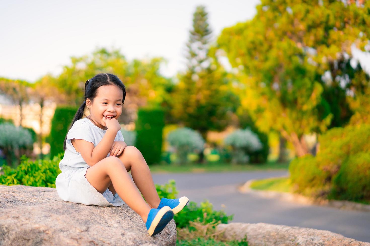 mooie kleine lachende meisje buiten zittend op grote rots foto