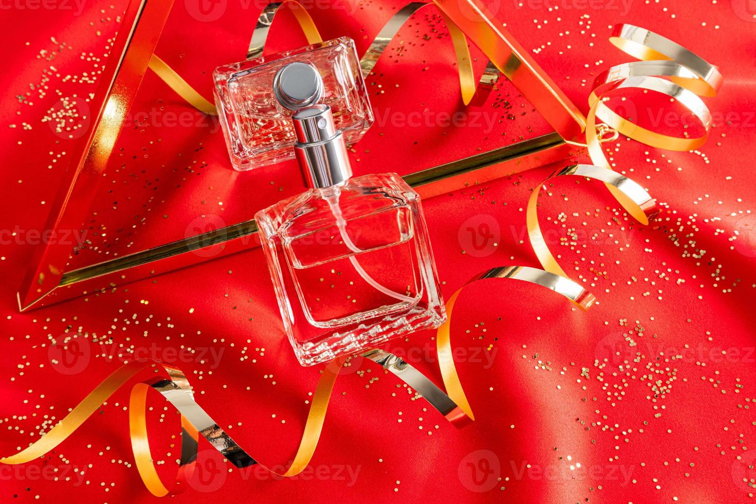 een chique parfum fles is weerspiegeld in een spiegel tegen van een gouden serpentijn. rood satijn achtergrond. nieuw jaar presentatie van de geur. foto