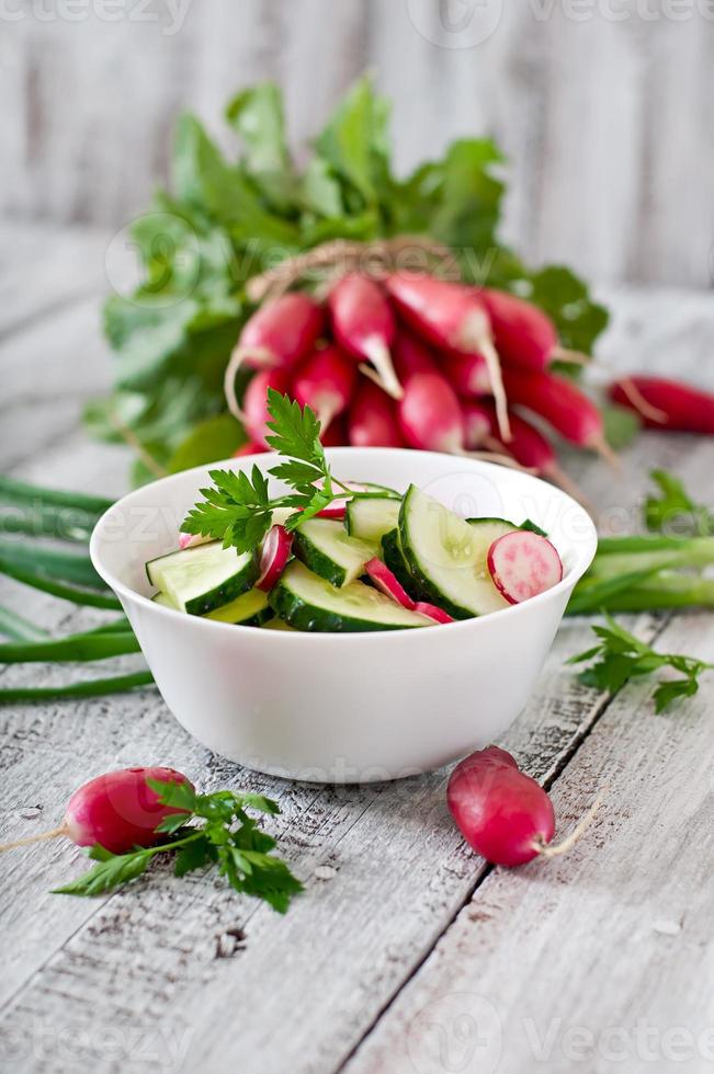 vers salade van komkommers en radijs in een wit kom Aan de oud houten achtergrond foto