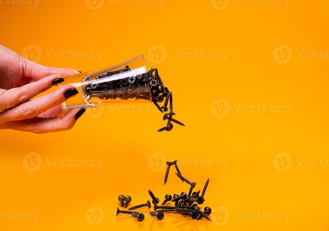 liet vallen veel metaal zelftappend schroeven gemaakt van staal in een glas, in emmer kan. zelftappend schroef voor metaal, voor ijzer, verchroomd zelftappend schroef, Aan een oranje geel achtergrond, foto