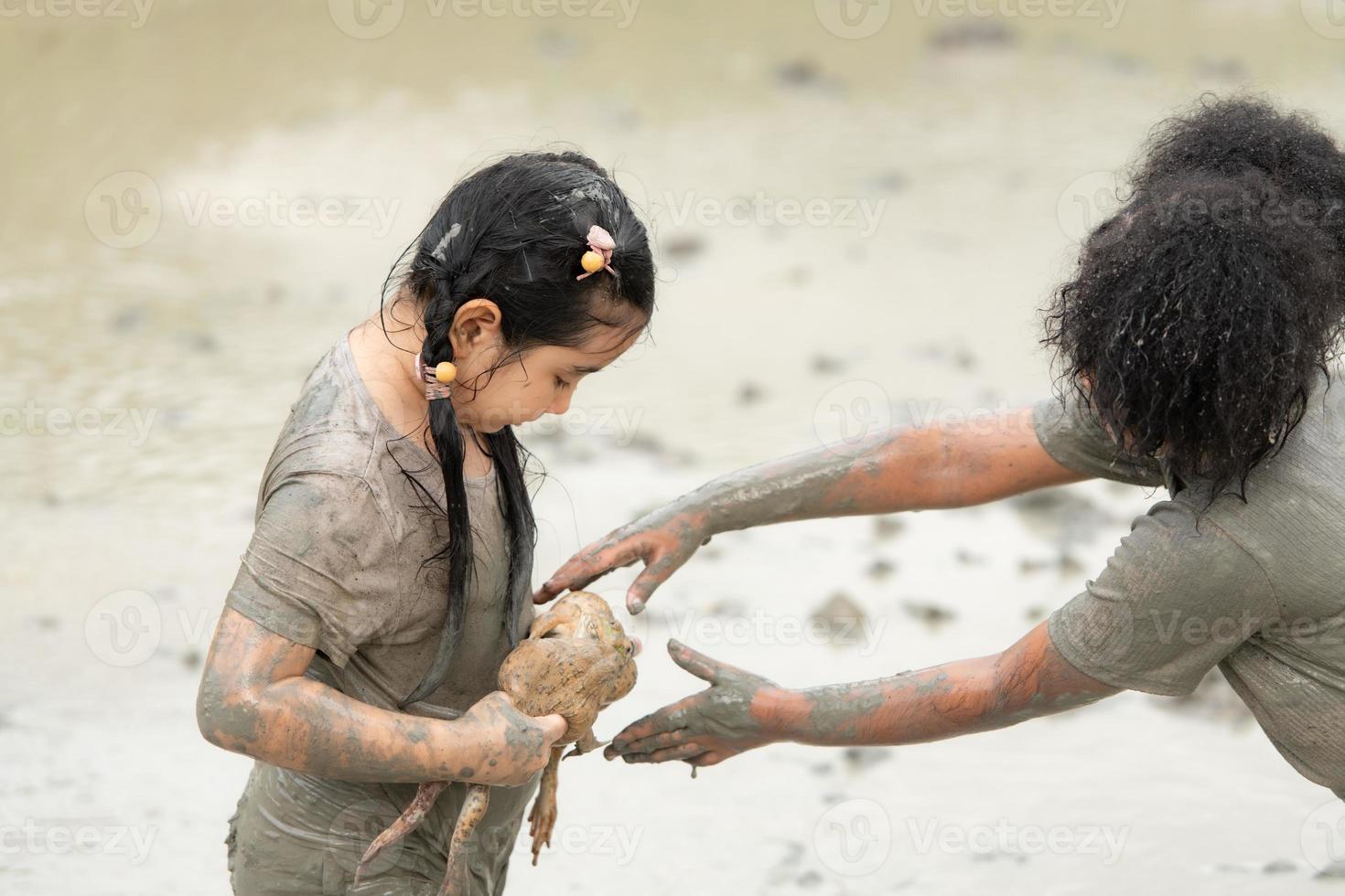 kinderen hebben pret spelen in de modder in de gemeenschap velden en vangen een kikker in een modderig veld. foto