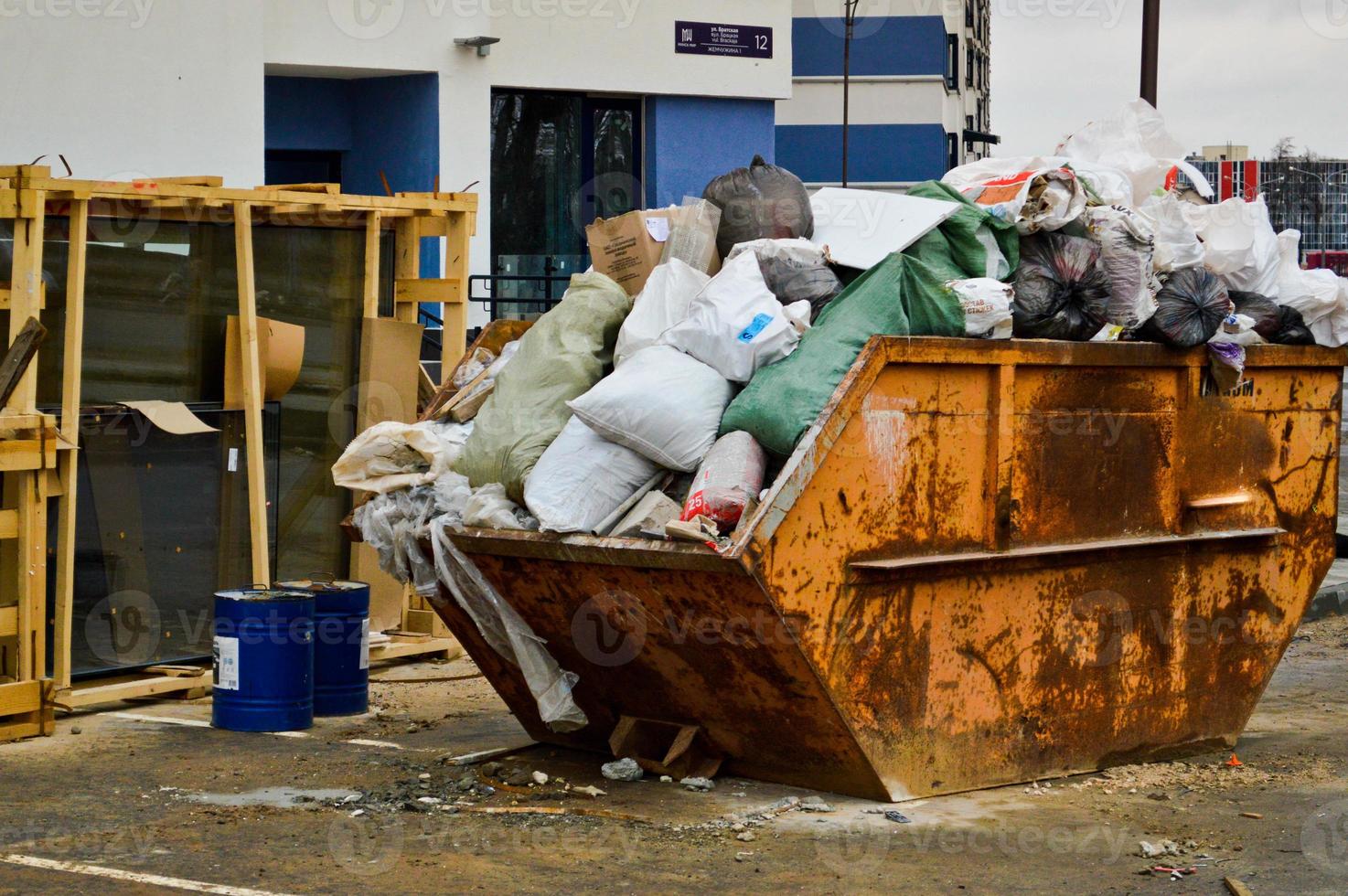 groot ijzer industrieel uitschot kan. een knoeien met vuilnis met aarde, arm veiligheid, onhygiënisch voorwaarden en milieu verontreiniging Bij een industrieel bouw plaats foto