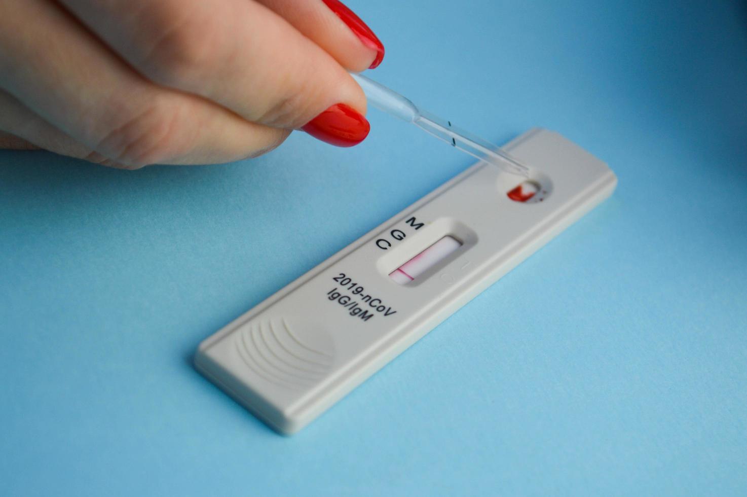 test voor coronavirus Aan een blauw achtergrond. meisje met een helder rood manicure maakt een bloed testen. een klein test buis is gedruppeld met een zoutoplossing oplossing op de test strip foto