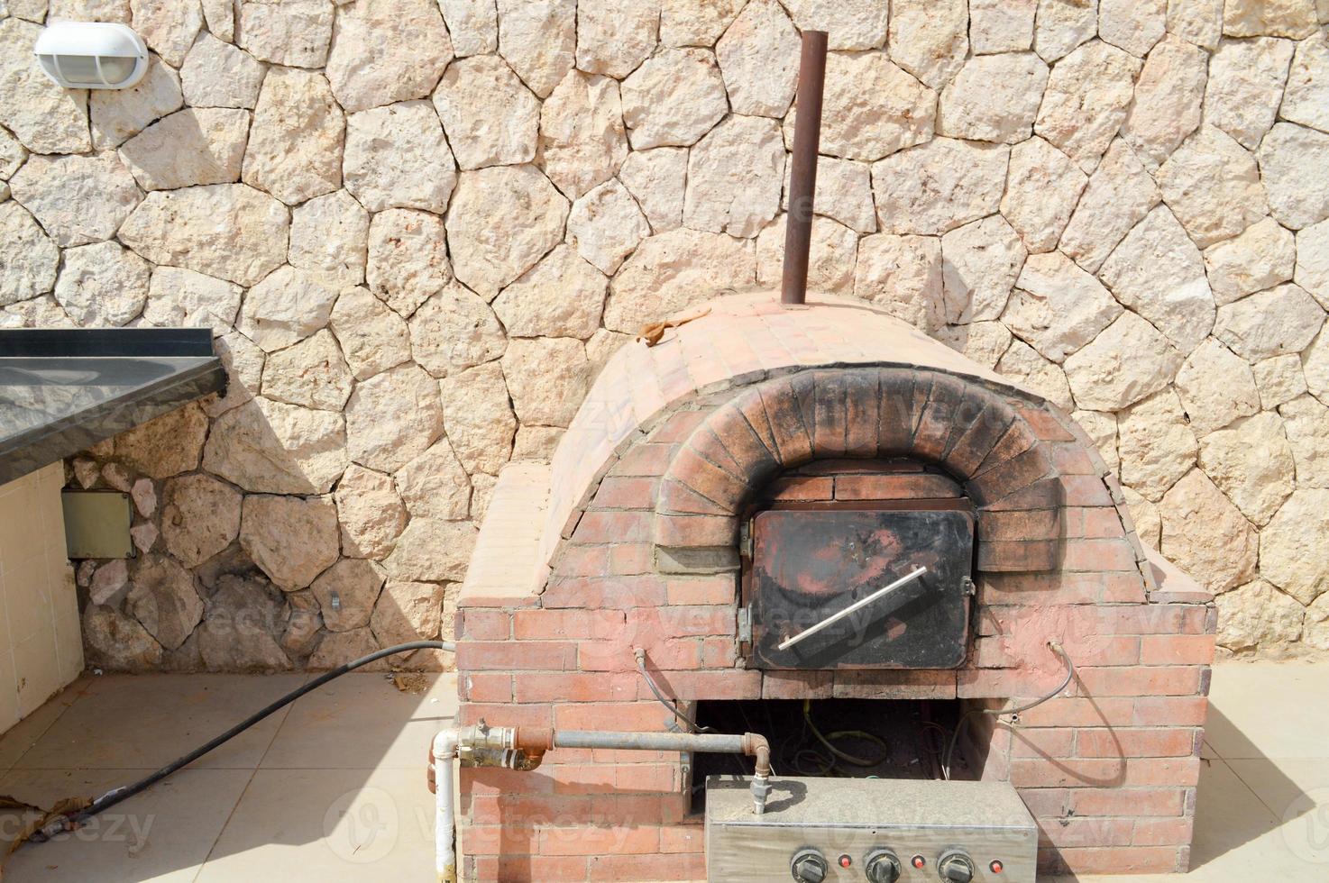 een groot professioneel industrieel bruin steen oven rooster oven met een buis voor Koken frituren voedsel van een steen betegeld Aan een steen muur achtergrond in de Open lucht straat foto