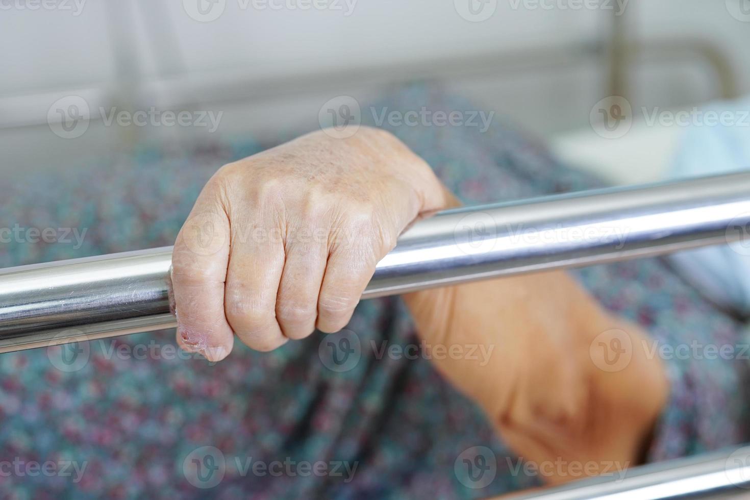 Aziatische oudere oudere vrouw die bedhek vasthoudt terwijl ze met hoop ligt te wachten op haar familie in het ziekenhuis. foto