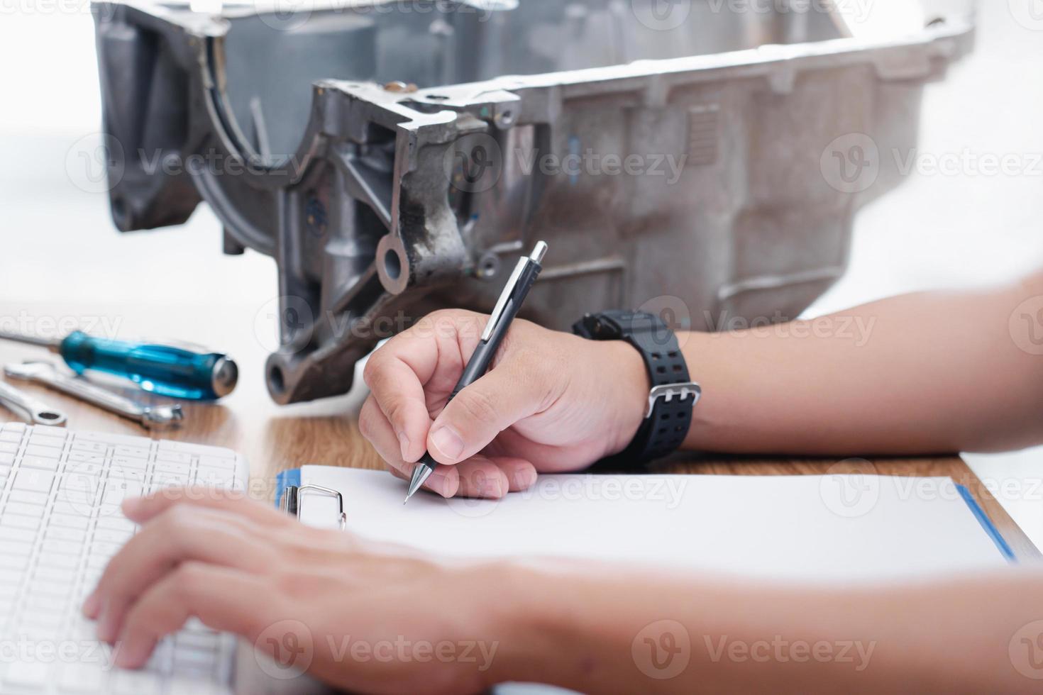 technicus schrijven Aan de wit papier klem bord het dossier en controleren beschadigd punt van de oud olie pan onderdelen controleren en reparatie beschadigd motoren en onderhoud concept foto