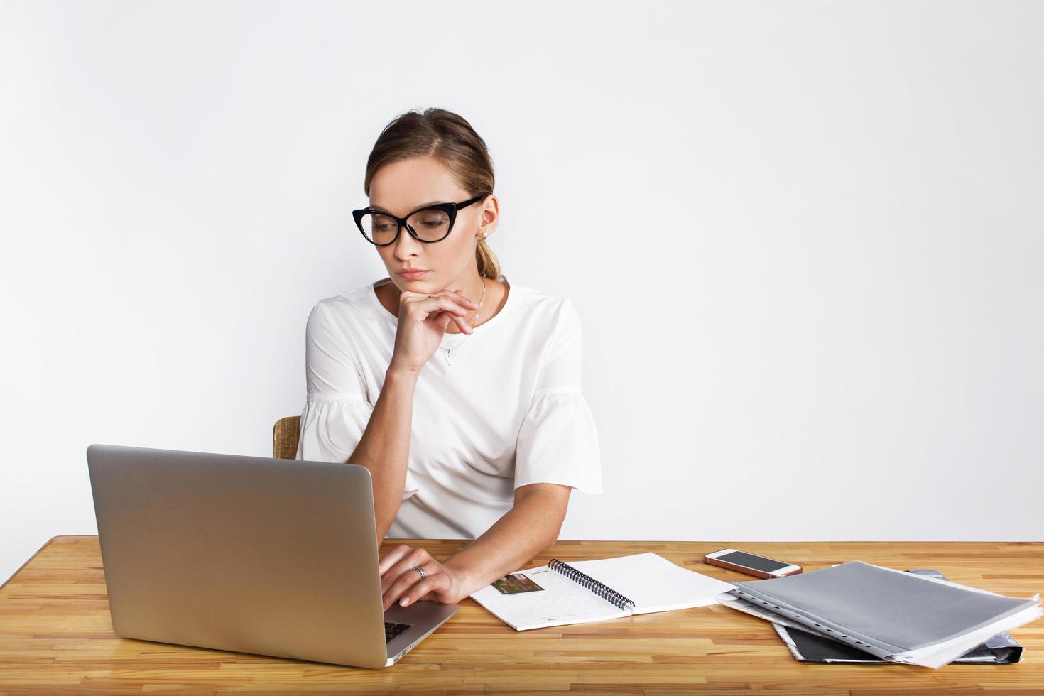 doordachte vrouw werkt op laptop aan bureau op witte achtergrond foto