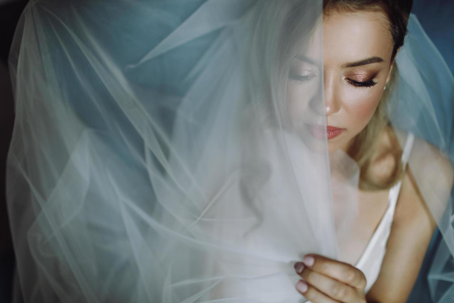 prachtige blonde bruid met diepe ogen verborgen onder blauwe sluier foto