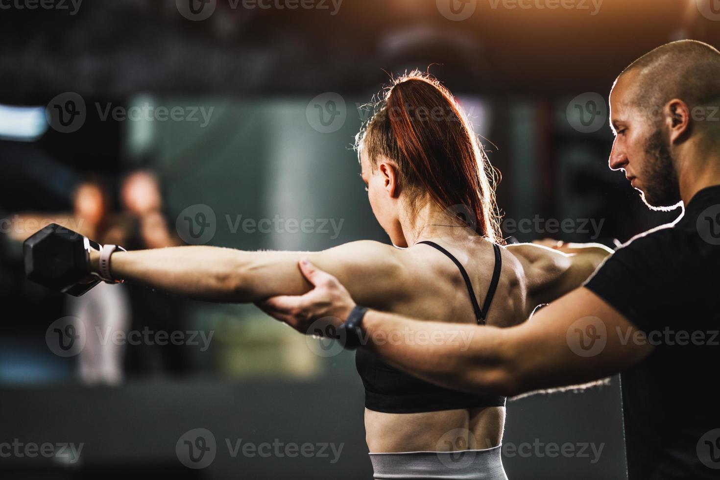 gespierd vrouw aan het doen moeilijk opleiding met persoonlijk trainer Bij de Sportschool foto