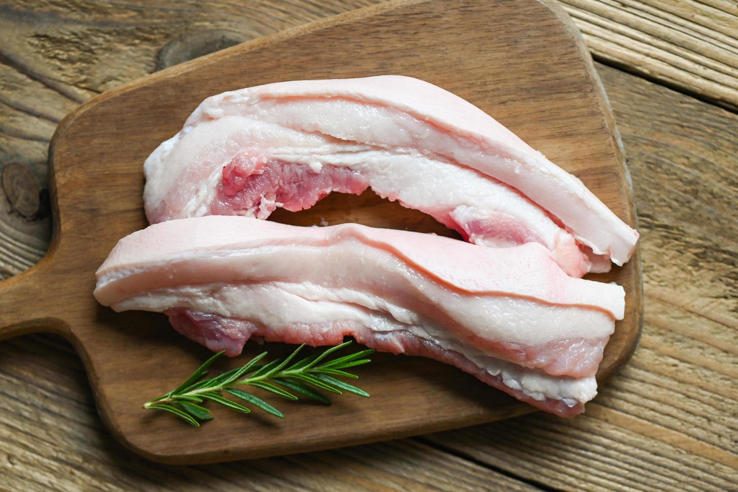 vers rauw buikspek varkensvlees vlees voor Koken voedsel, varkensvlees Aan houten bord met rozemarijn, varkensvlees huid varken huid foto