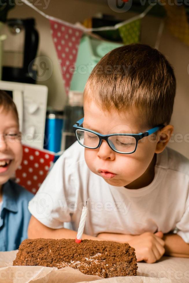 jongen van 7 jaren oud slagen uit de kaars Aan de taart. vieren verjaardag Bij huis. huis vakantie voor kinderen. portret van een jongen blazen Aan een kaars. maken een wens. foto