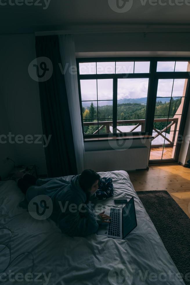 jong vrouw werken Aan laptop terwijl aan het liegen Aan bed foto