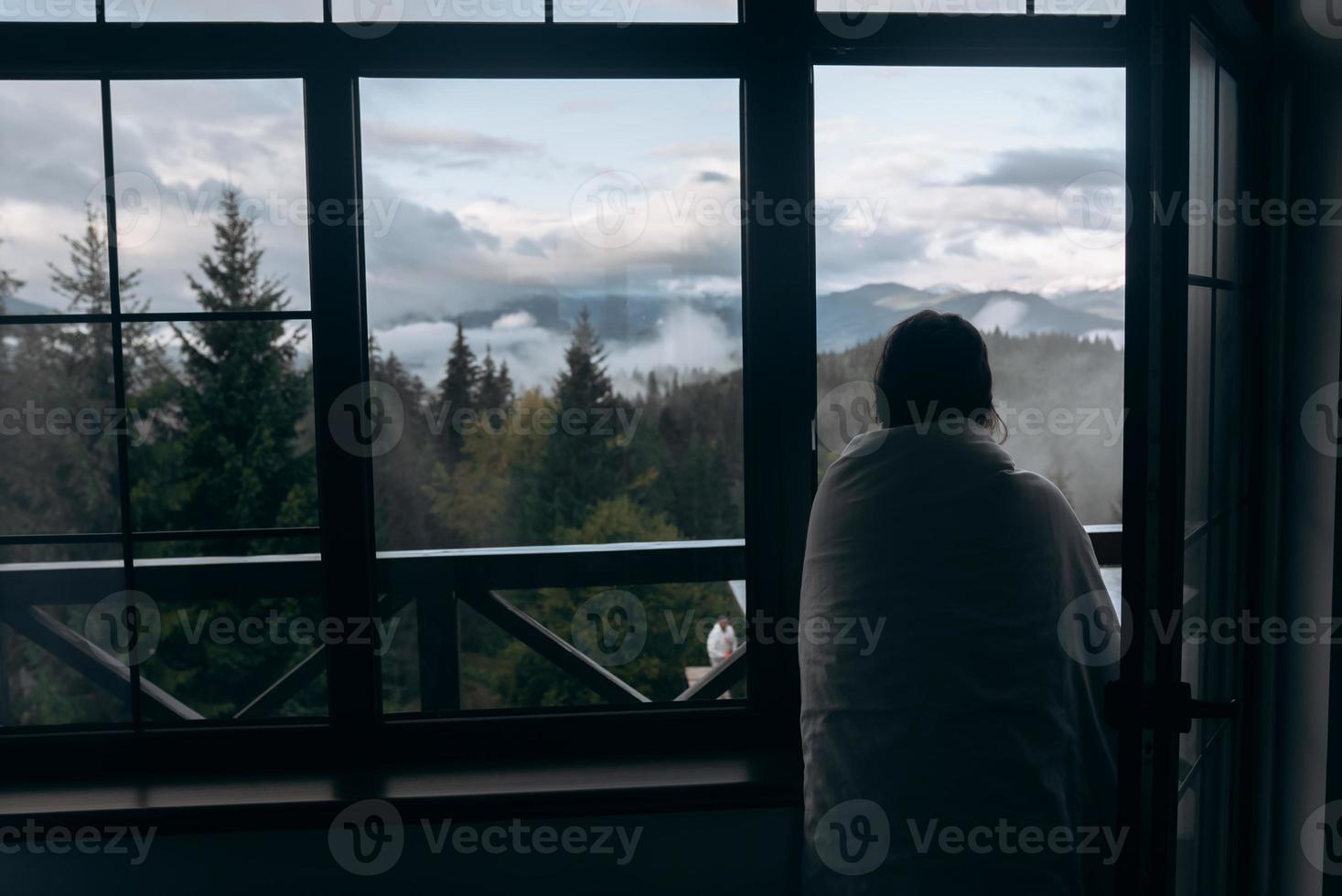 jong vrouw is op zoek door de venster Bij de bergen foto