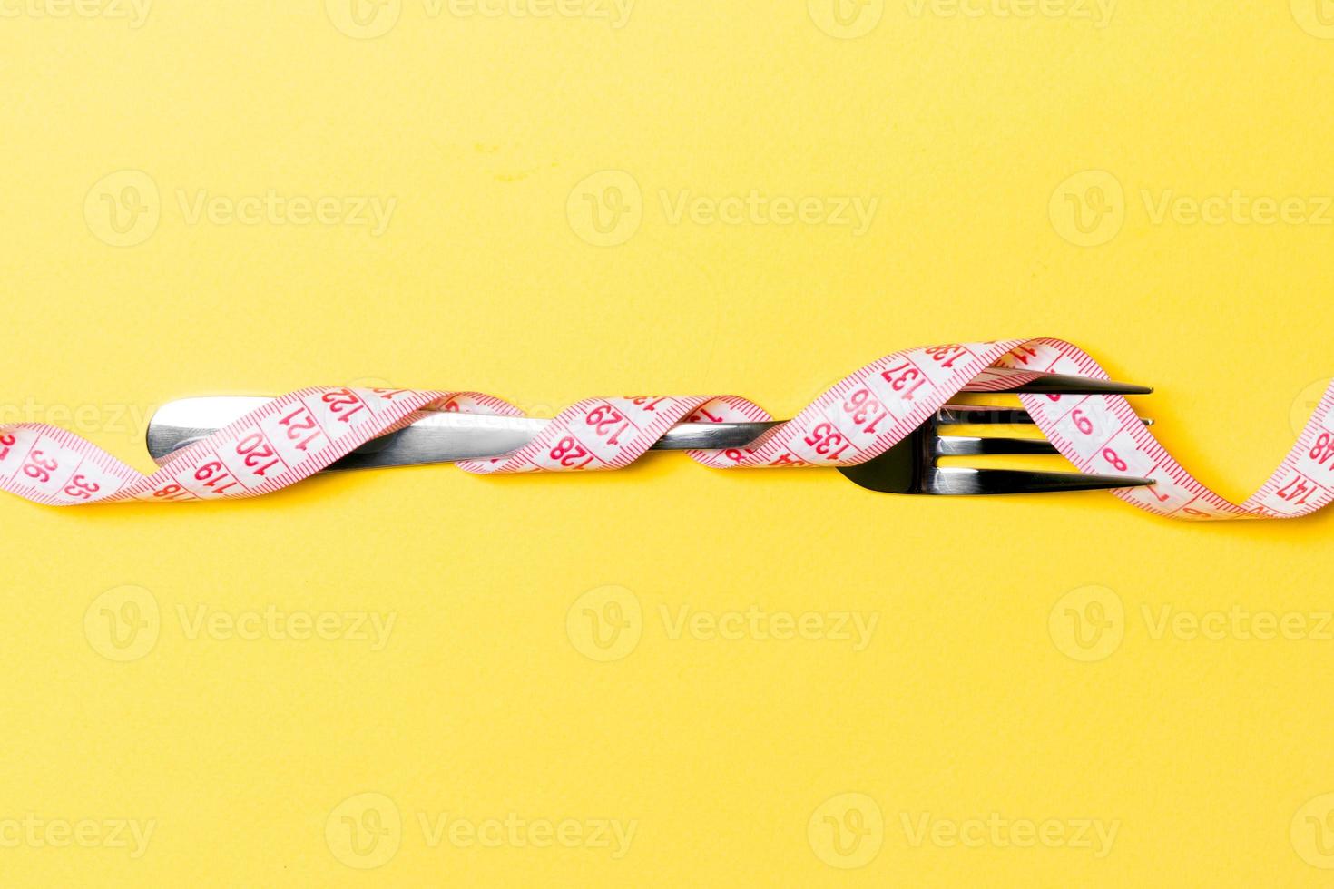 samenstelling van gekruld verpakt meten plakband en vork Aan geel achtergrond. te zwaar concept foto