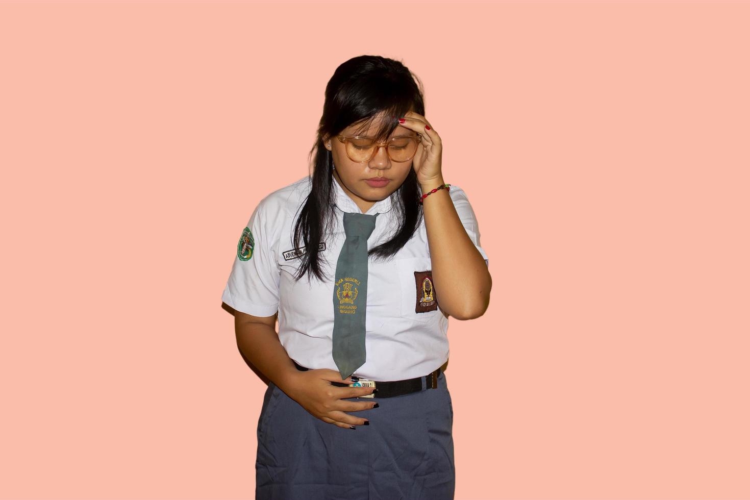 een Indonesisch vrouw hoog school- leerling vervelend een grijs wit overhemd uniform met een grijs stropdas lijdt van hoofdpijn en buikpijn foto