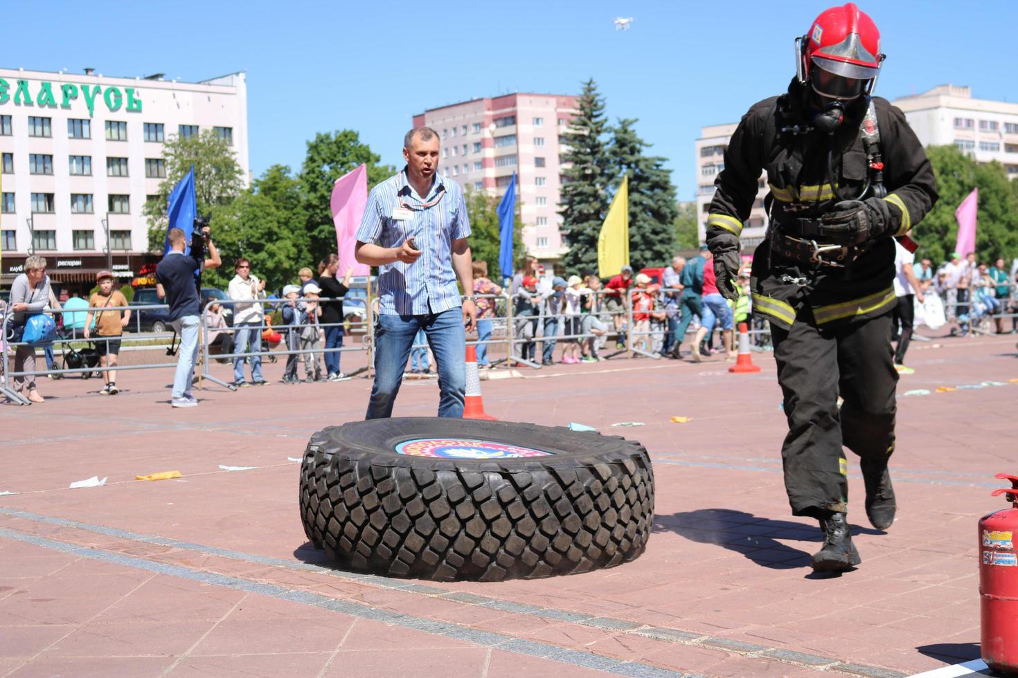 een brandweerman in een vuurvast pak en een helm loopt en bochten een groot rubber wiel in een brand vechten wedstrijd, Wit-Rusland, Minsk, 08.08.2018 foto