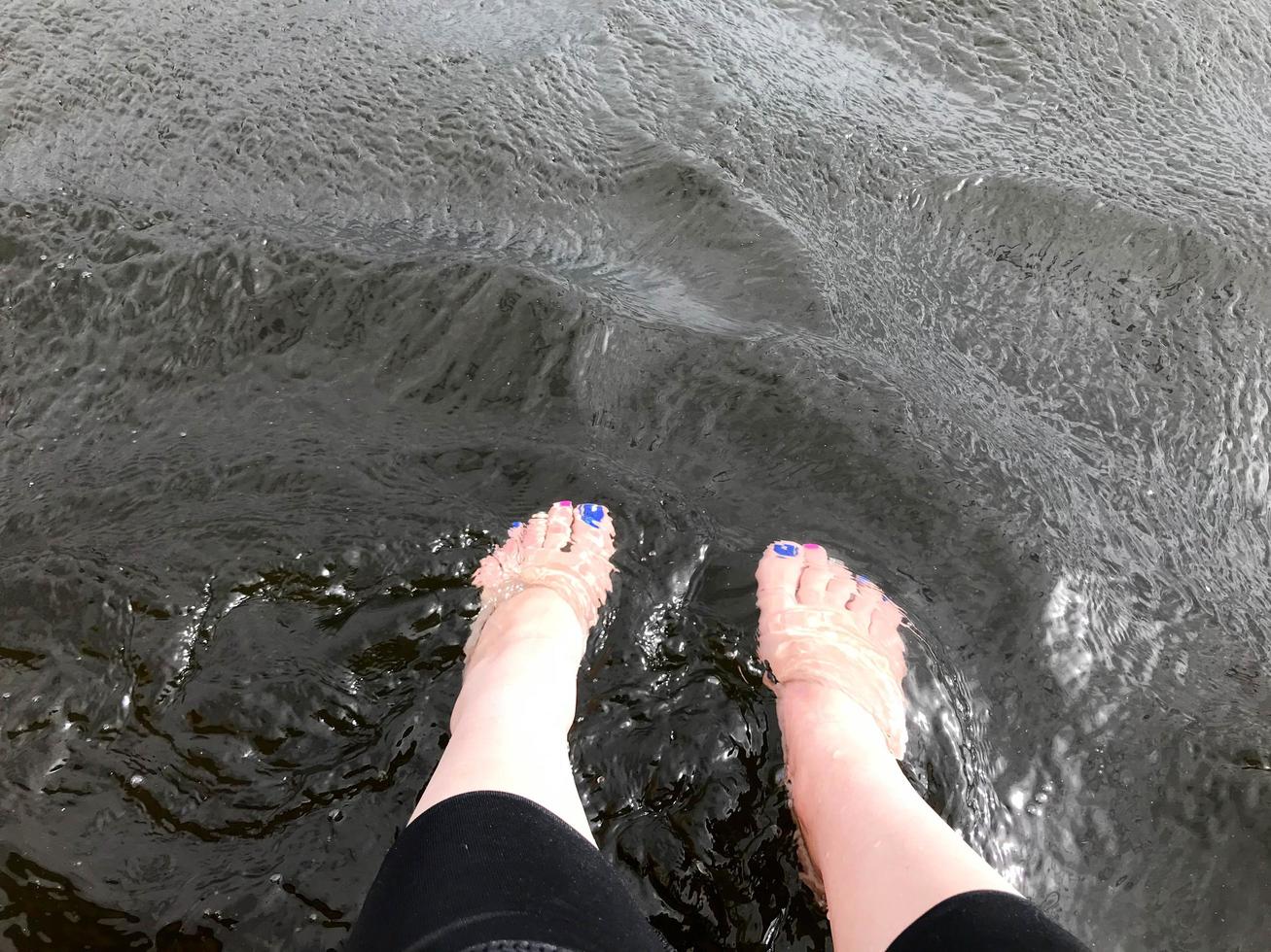 mooi vrouw voeten van de voeten met vingers met een veelkleurig mode manicure zijn liet vallen bungelend in verkoudheid donker zwart water foto