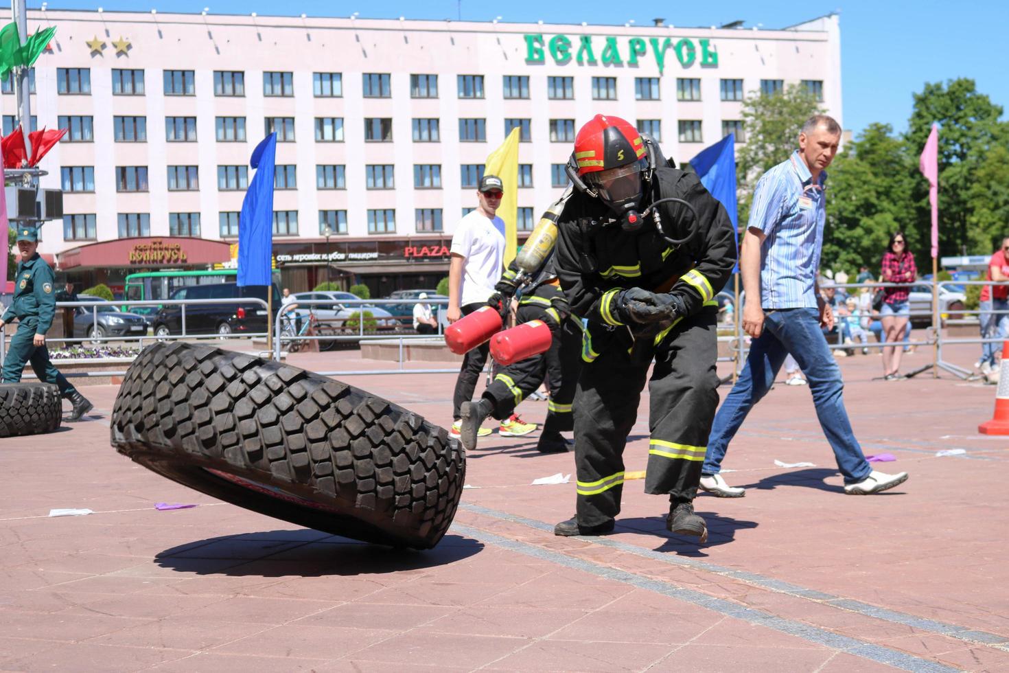 een brandweerman in een vuurvast pak en een helm loopt en bochten een groot rubber wiel in een brand vechten wedstrijd, Wit-Rusland, Minsk, 08.08.2018 foto