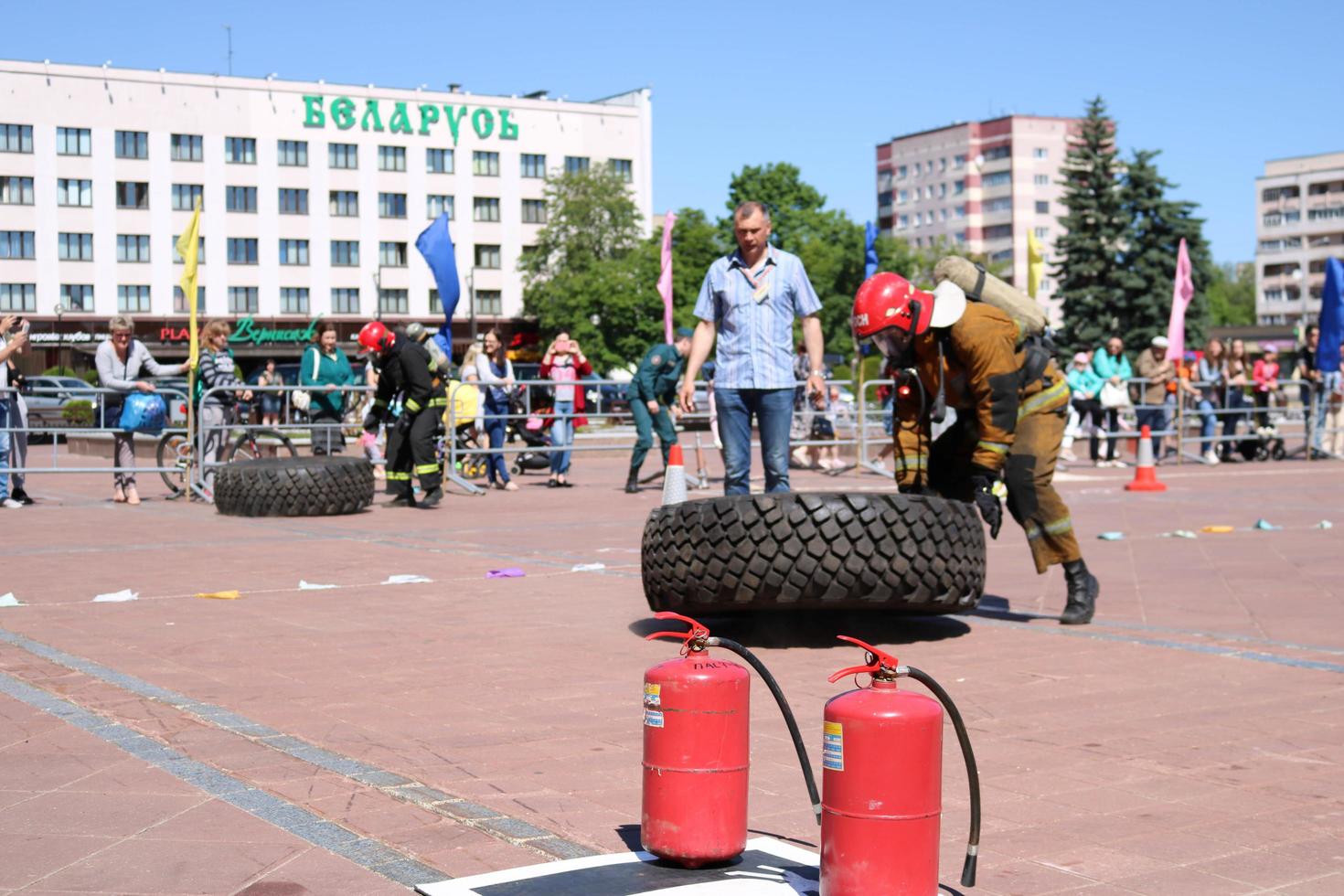 een brandweerman in een vuurvast pak en een helm loopt en bochten een groot rubber wiel in een brand vechten wedstrijd, Wit-Rusland, Minsk, 08.08.2018 foto