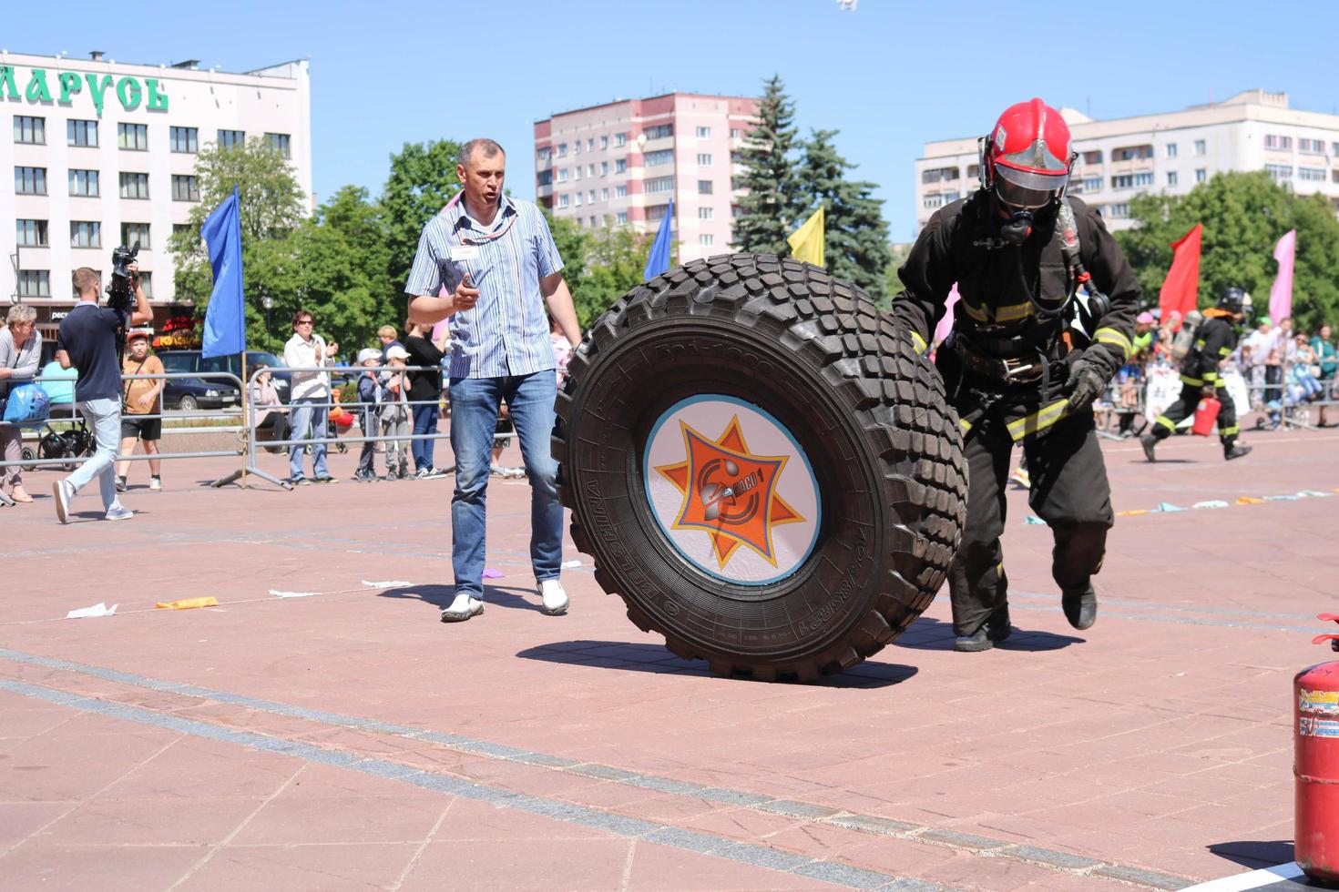 een brandweerman in een vuurvast pak en een helm loopt en bochten een groot rubber wiel in een brand vechten wedstrijd, Wit-Rusland, Minsk, 08.08.2018 foto