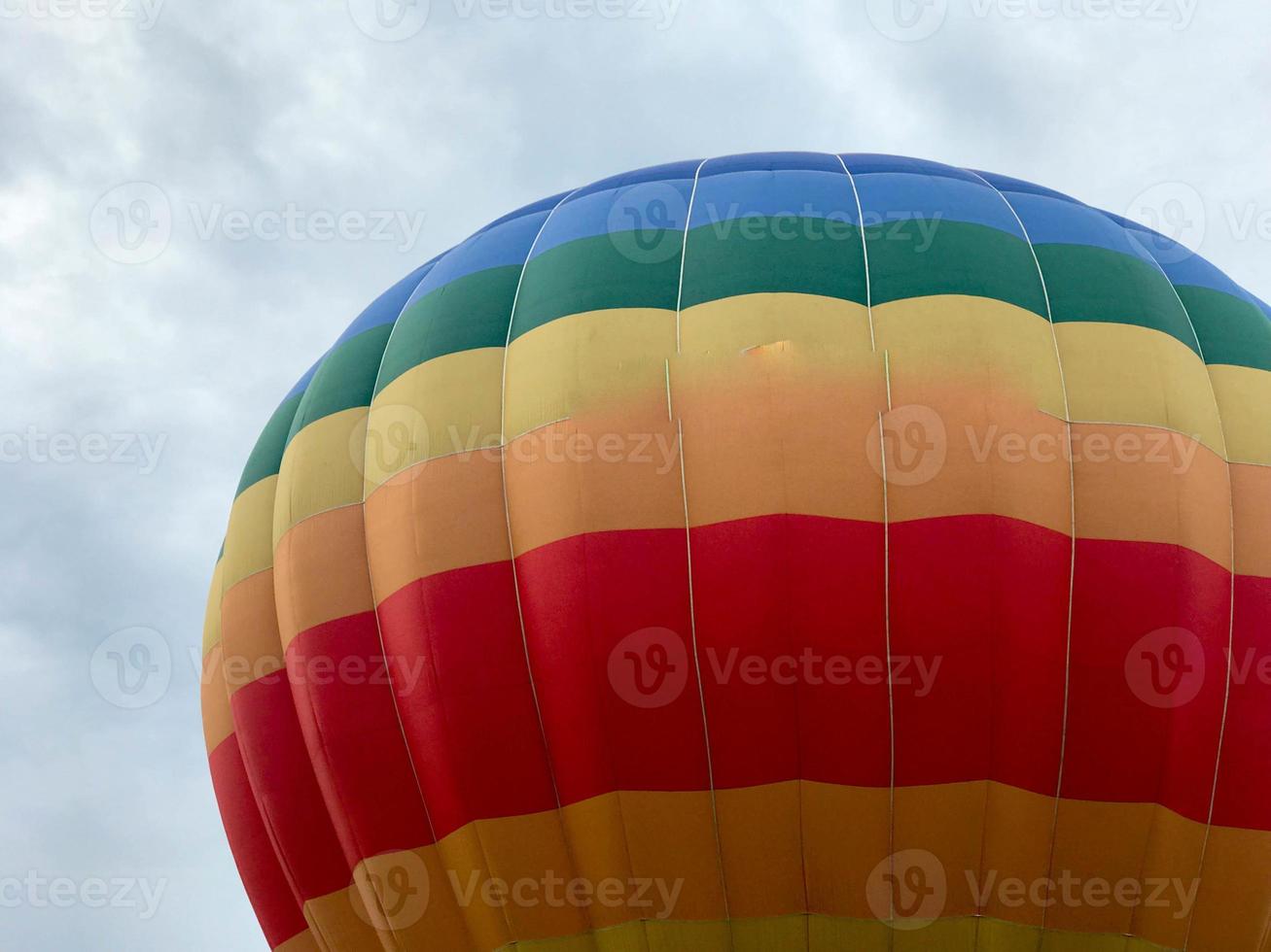 groot veelkleurig helder ronde regenboog gekleurde gestreept gestreept vliegend ballon met een mand tegen de lucht in de avond foto