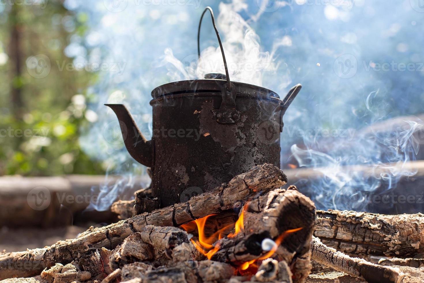 koken waterkoker met heet drinken staat Aan een kampvuur in de rook, in een Woud. foto