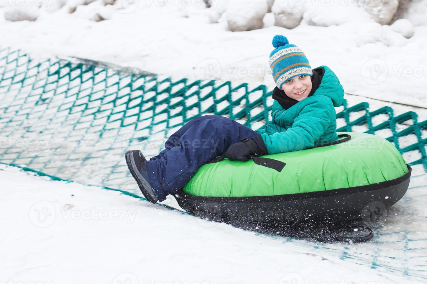 kind hebben pret Aan sneeuw buis. jongen is rijden een buizen. winter amusement. kind glijden bergafwaarts Aan buis foto