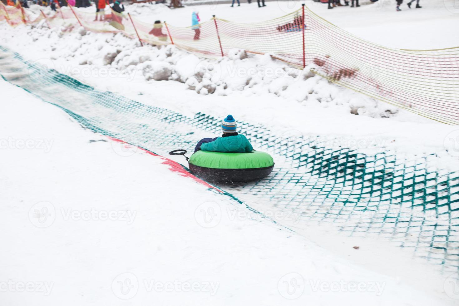 kind hebben pret Aan sneeuw buis. jongen is rijden een buizen. winter amusement. kind glijden bergafwaarts Aan buis foto