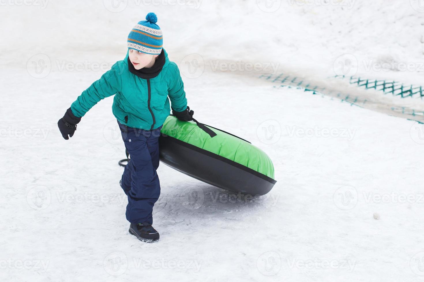 kind hebben pret Aan sneeuw buis. jongen is rijden een buizen. winter amusement. kind slepen slangen foto