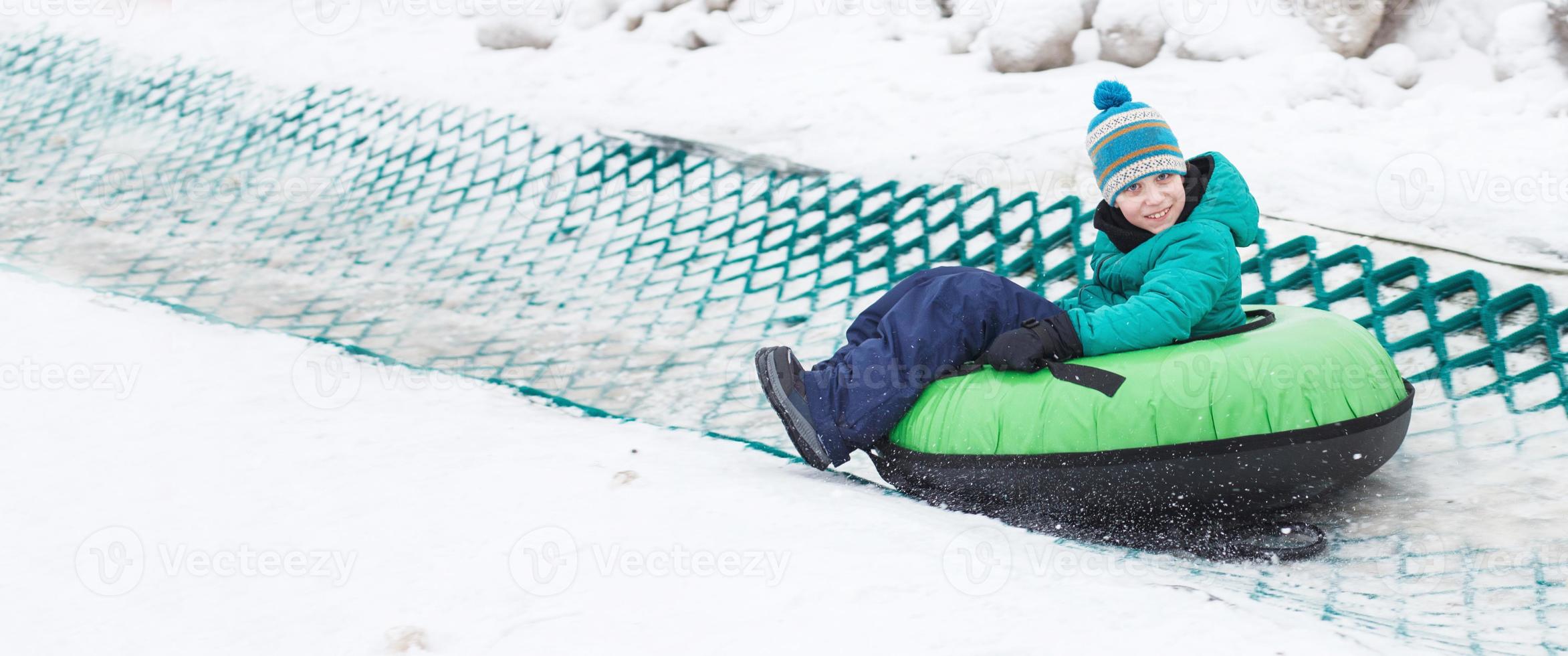 kind hebben pret Aan sneeuw buis. jongen is rijden een buizen. winter amusement. kind glijden bergafwaarts Aan buis. banier foto