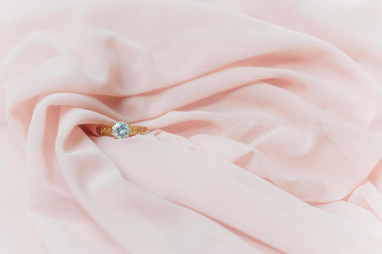 dichtbij omhoog van diamant ring Aan roze kleding stof voor Valentijn dag of bruiloft achtergrond foto