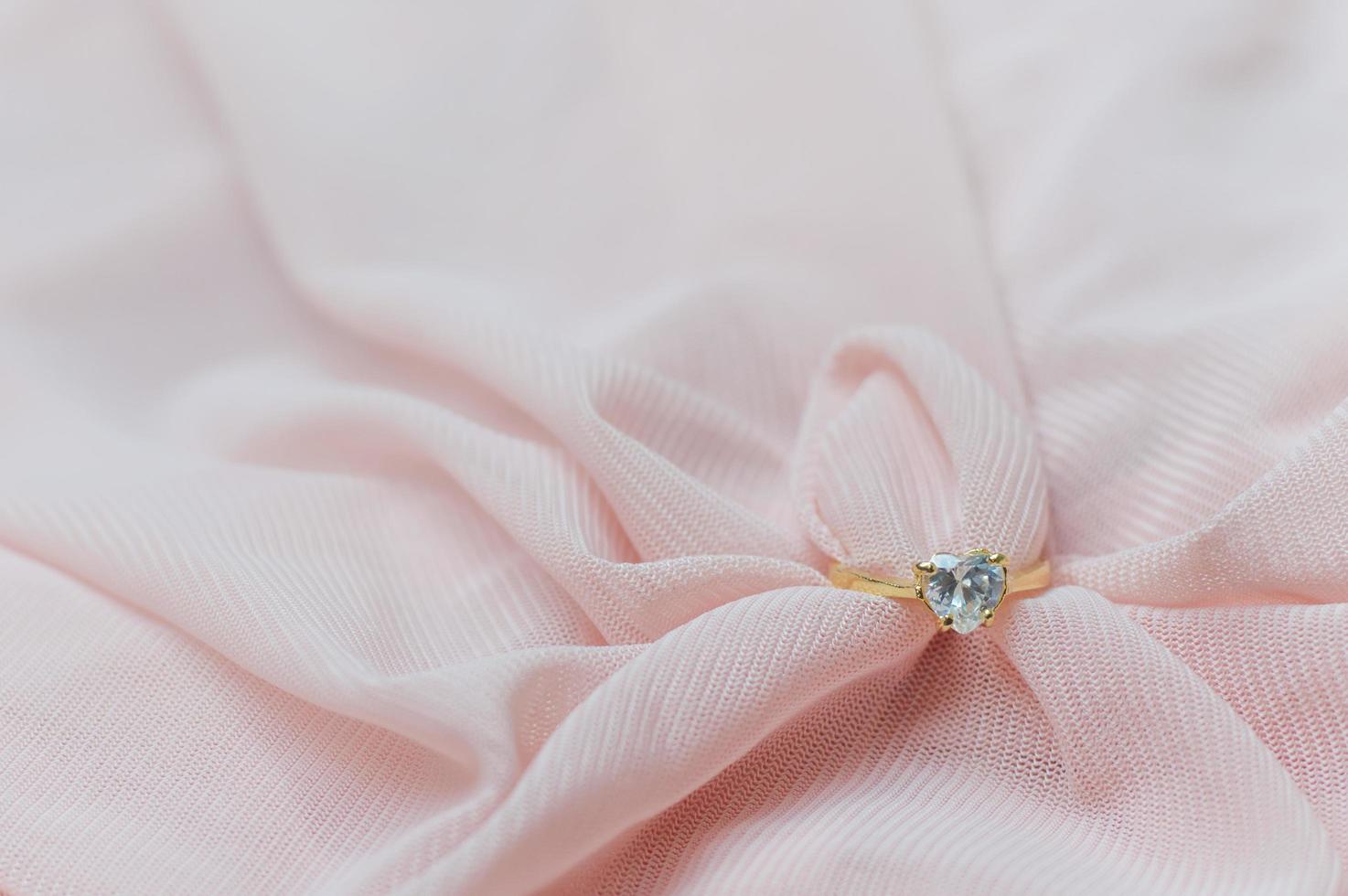 dichtbij omhoog van diamant ring Aan roze kleding stof voor Valentijn dag of bruiloft achtergrond foto