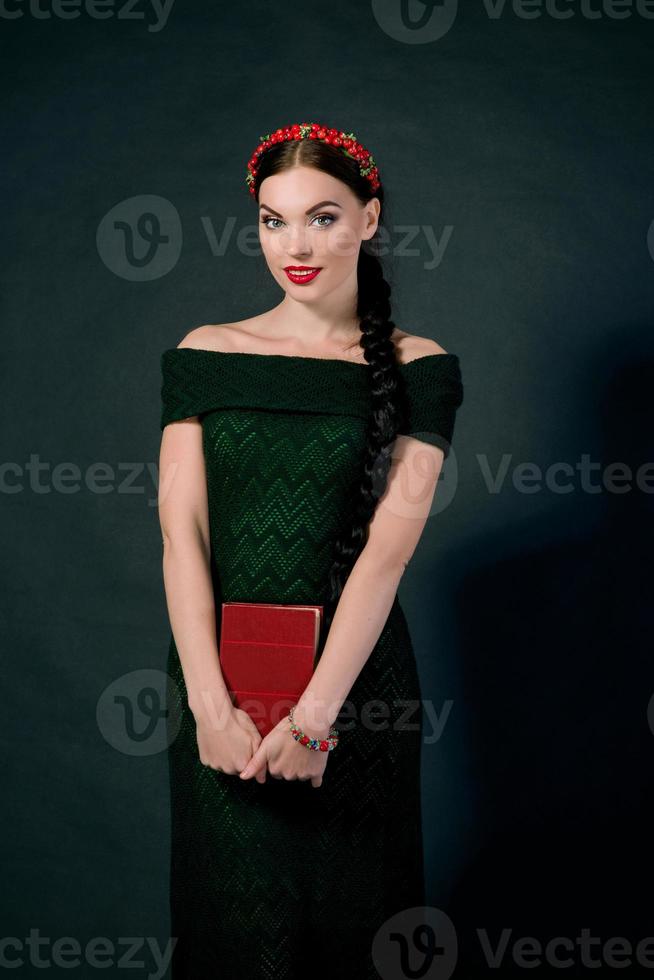 portret van glimlachen jong mooi brunette met rood krans en vlecht Aan donker achtergrond foto