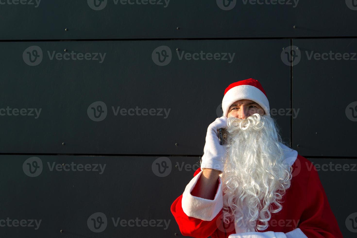 modern de kerstman claus pratend Aan de telefoon. bestellen de Diensten van een animator voor de Kerstmis en nieuw jaar. online groeten via de internet en mobiel communicatie, sociaal afstand foto