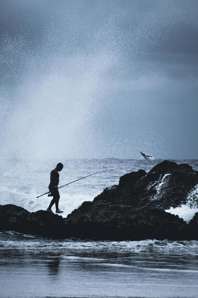 sydney, australië, man staande op rotsen in de buurt van de oceaan met een hengel foto