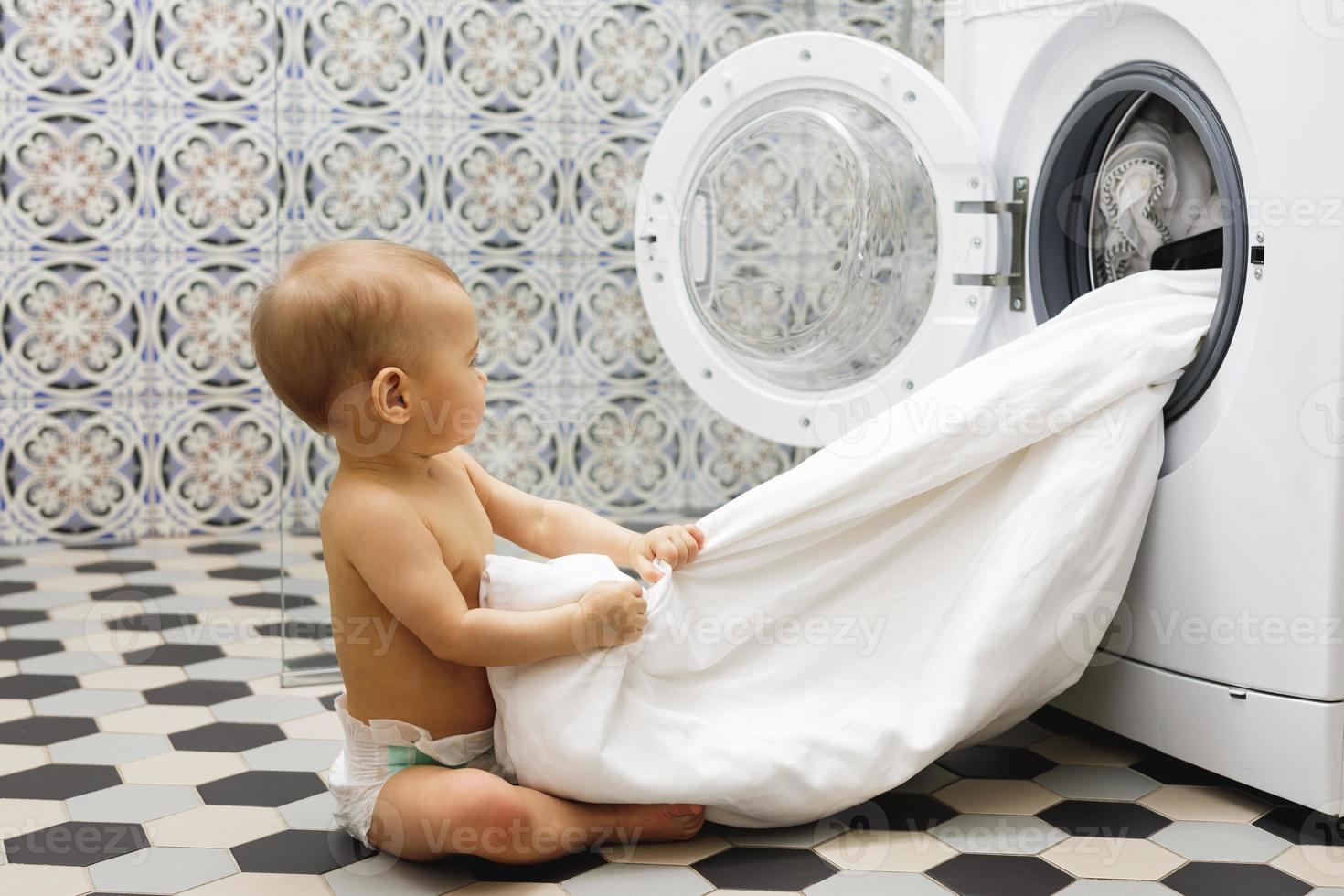 schattig baby jongen naast de het wassen machine foto