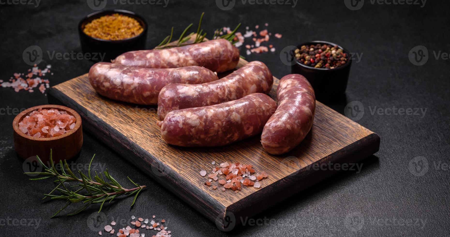 rauw varkensvlees worstjes rooster met specerijen en kruiden Aan een donker beton tafel foto