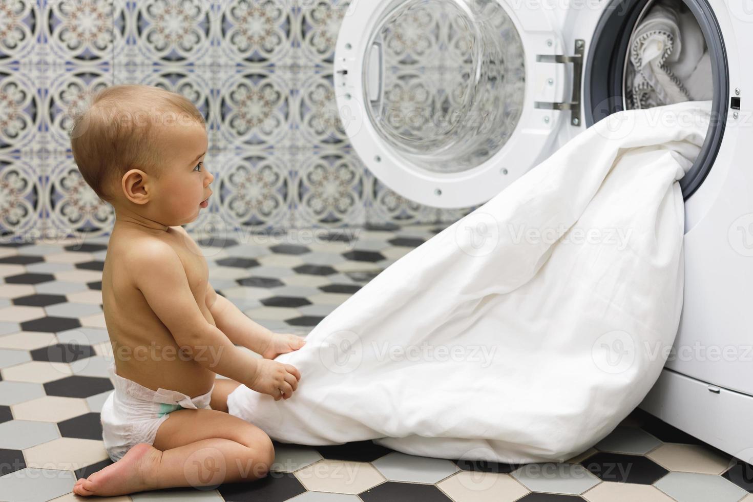 schattig baby jongen naast de het wassen machine foto