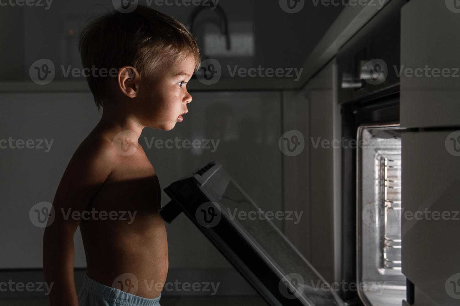nieuwsgierig baby jongen opent de heet oven. concept van veiligheid en mogelijk problemen met onbeheerd kinderen. foto