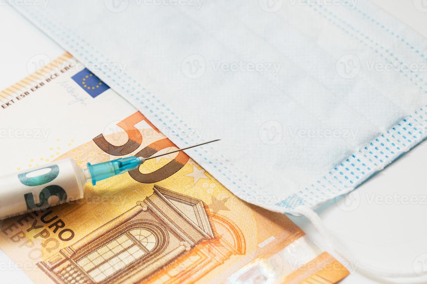 plastic injectiespuit gevulde met gerold papier geld, vijftig euro bankbiljet en beschikbaar hygiënisch gezicht masker. foto