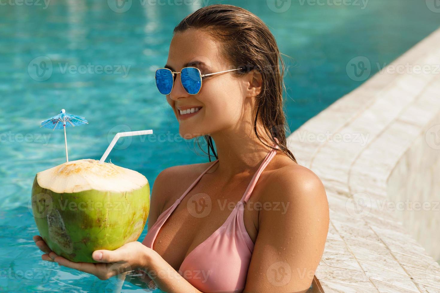 vrouw ontspannende in de zwemmen zwembad en drinken kokosnoot water foto