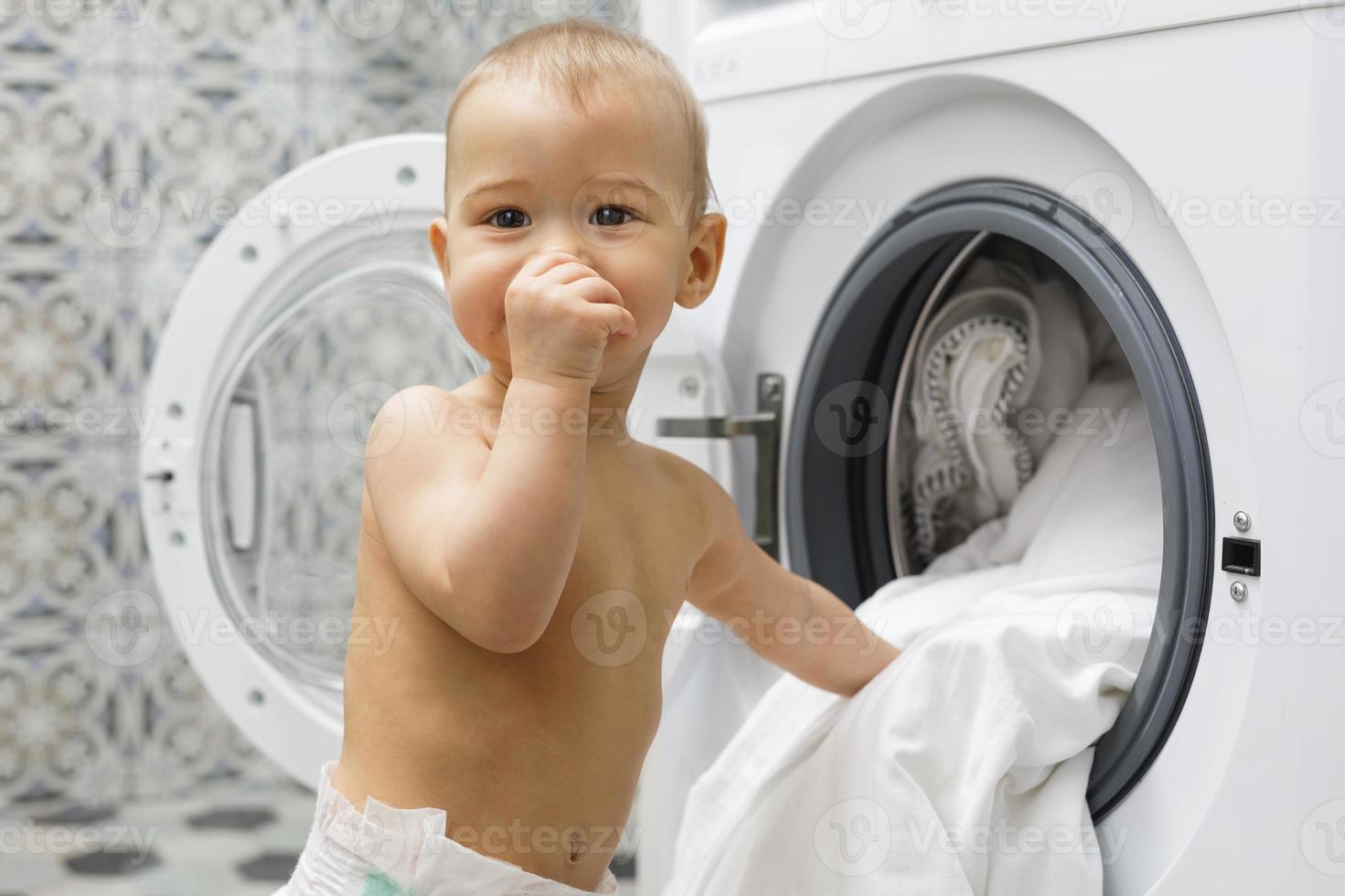 schattig baby jongen naast de het wassen machine foto