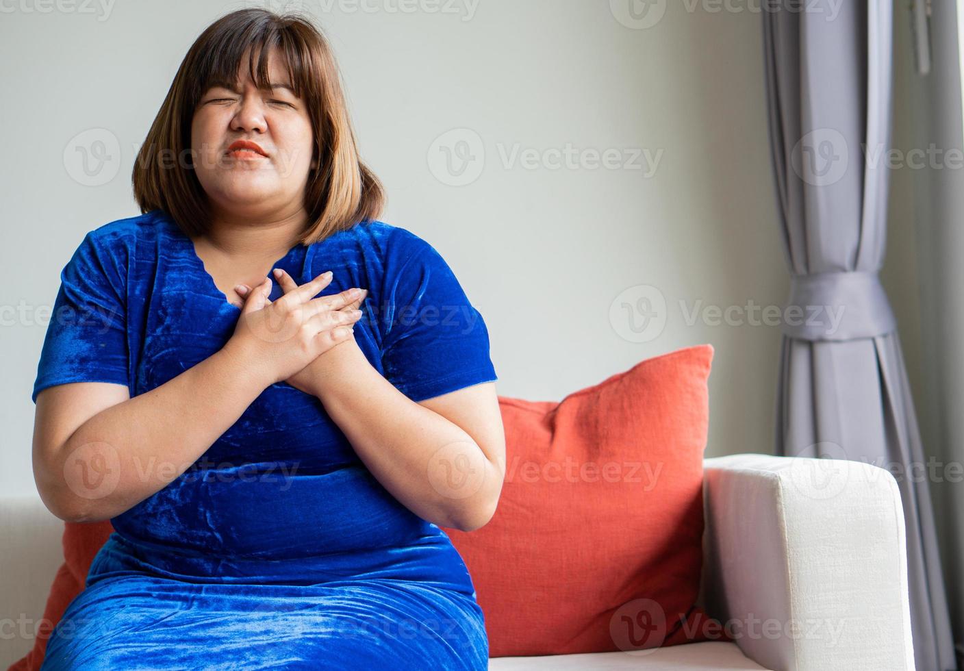 te zwaar Aziatisch Dames zijn zittend Aan de sofa in de leven kamer. en handvatten in de borst ten gevolge naar hart ziekte, ziekte, en Gezondheid zorg concept. foto