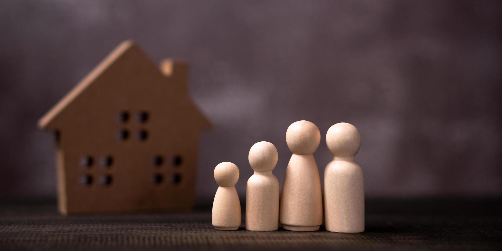 houten figuren familie staand in voorkant van een houten huis. de concept van bescherming en veiligheid, huis veiligheid, eigendom verzekering en huis. foto