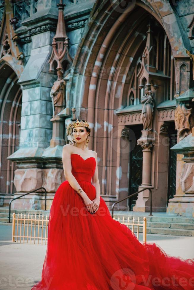 mooi vrouw in lang rood jurk en in Koninklijk kroon bijna Katholiek kathedraal foto