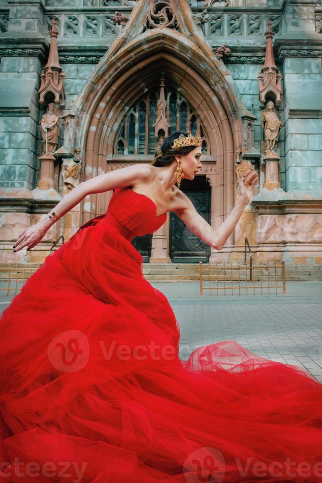 mooi vrouw in lang rood jurk en in Koninklijk kroon bijna Katholiek kathedraal foto