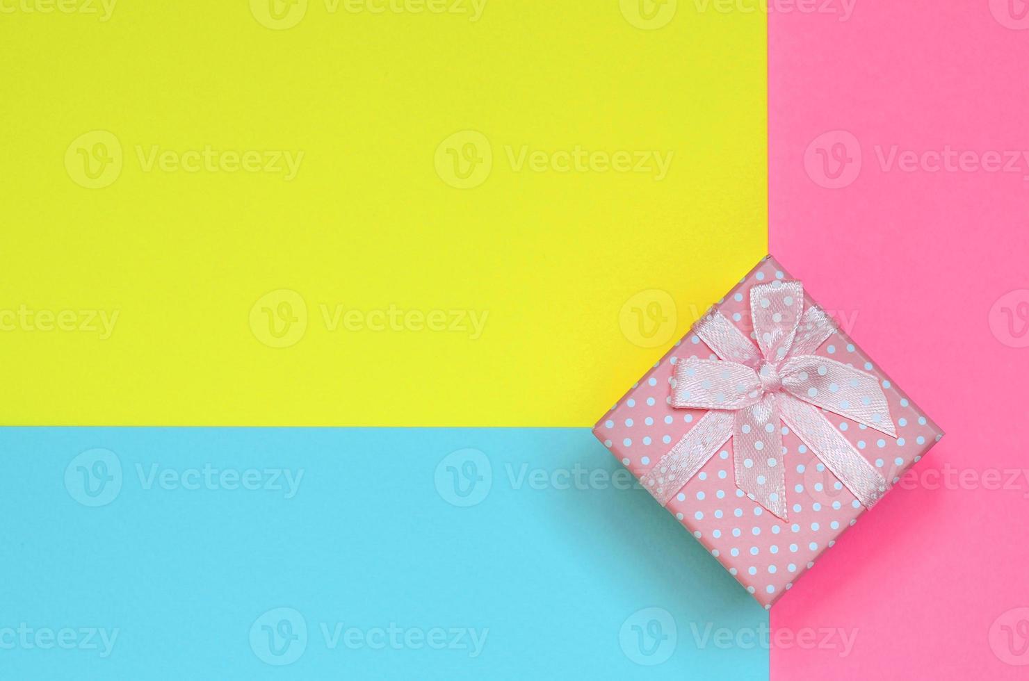 klein roze geschenk doos liggen Aan structuur achtergrond van mode pastel blauw, geel en roze kleuren papier in minimaal concept foto