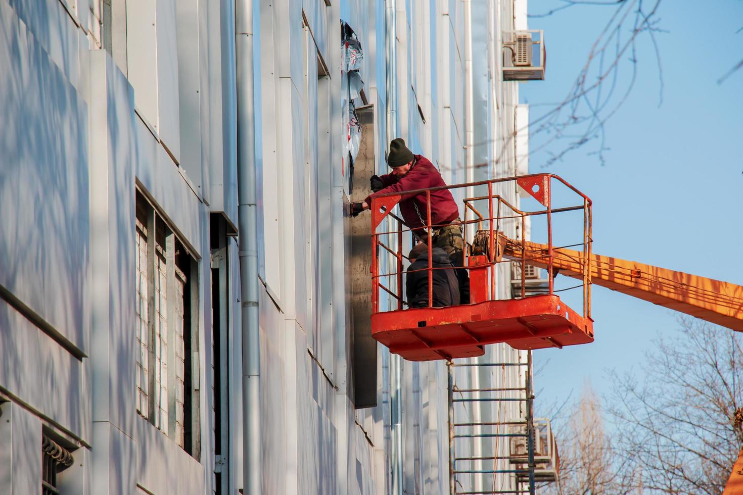 dnepropetrovsk, Oekraïne - 02.09.2022 bouwer in een kraan mand reparaties de coating van een metaal structuur Aan de muur van de facade van een gebouw. foto