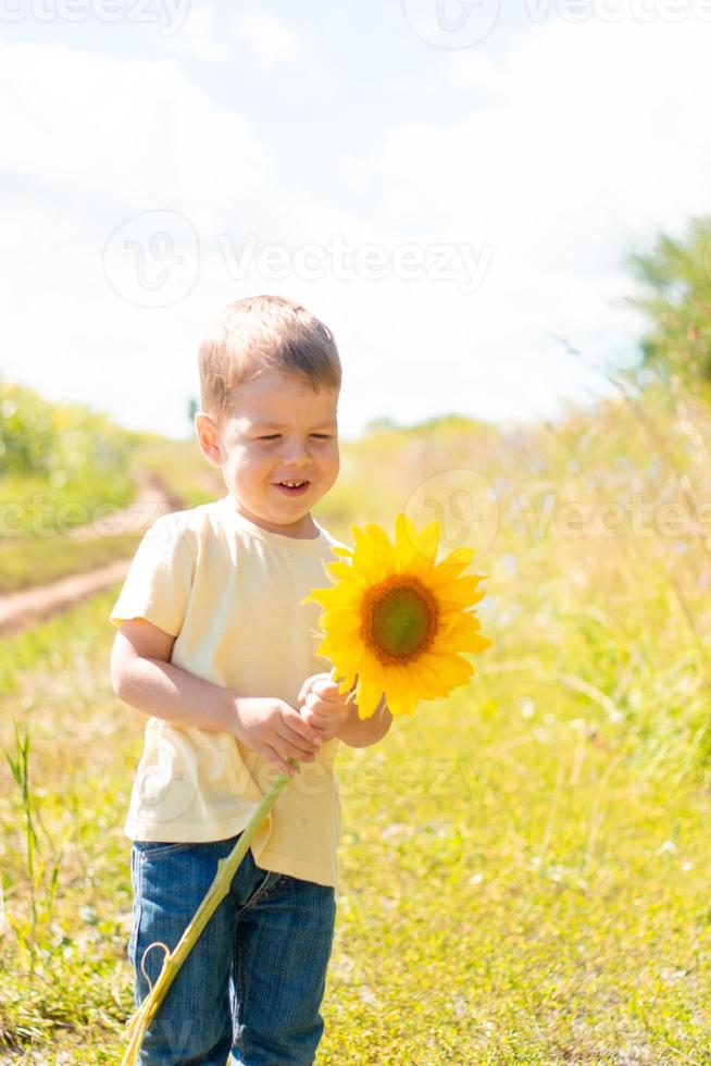 weinig schattig jongen in een veld- van zonnebloemen in een geel t-shirt staat en glimlacht. foto